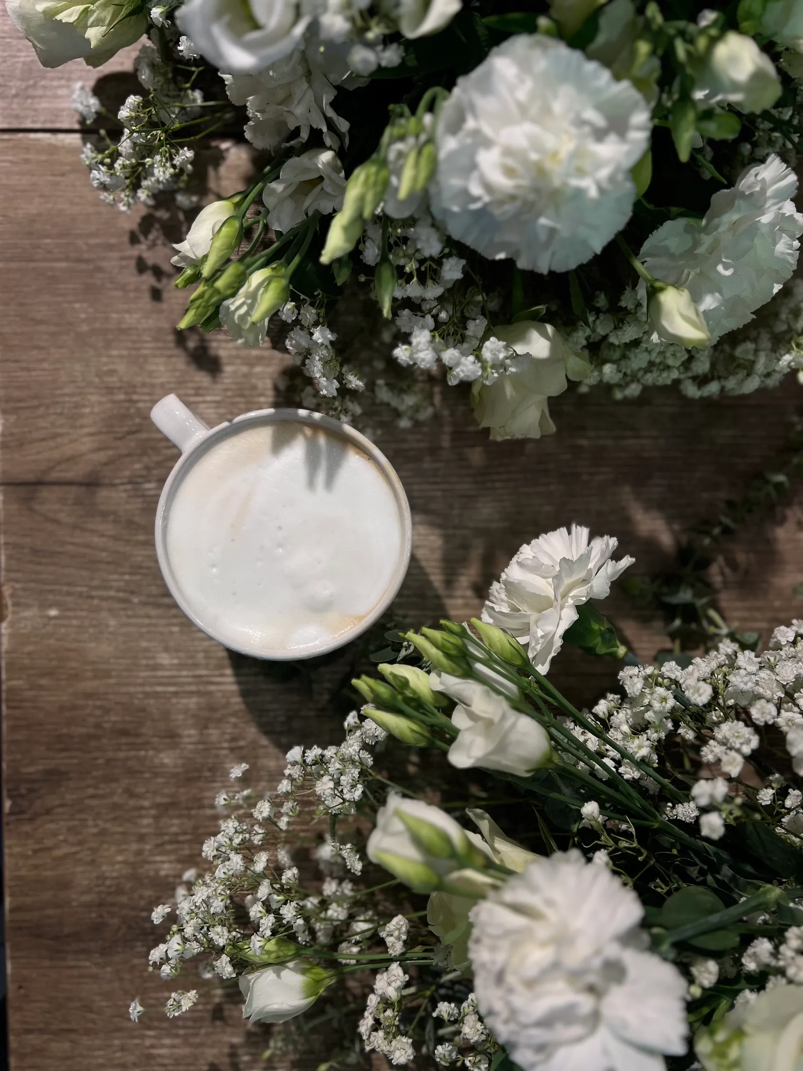Kaffeetasse zwischen weißen Nelken und Schleierkraut auf der Werkbank