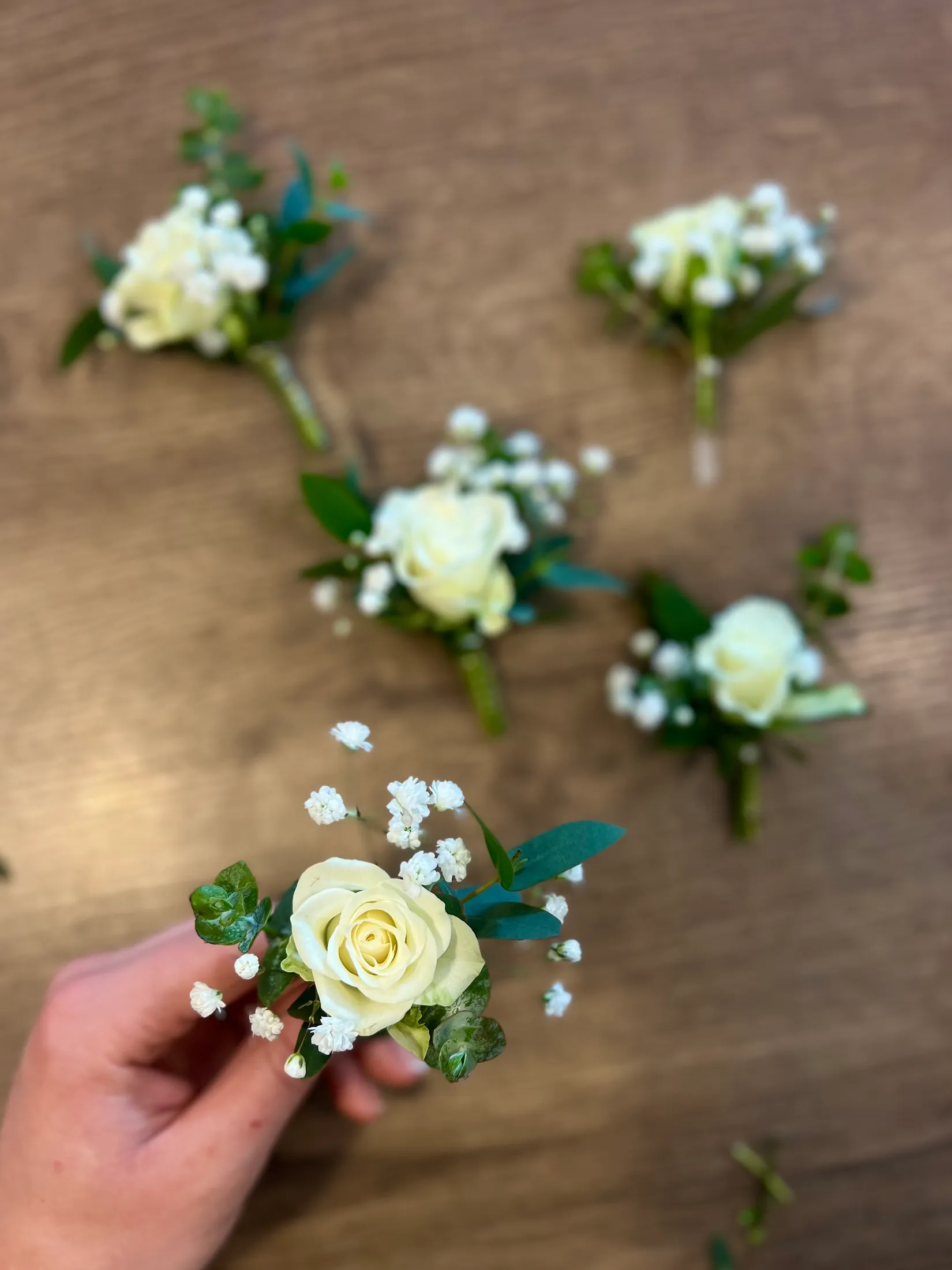 Ansteckblumen aus weißen Rosen auf einem Holztisch